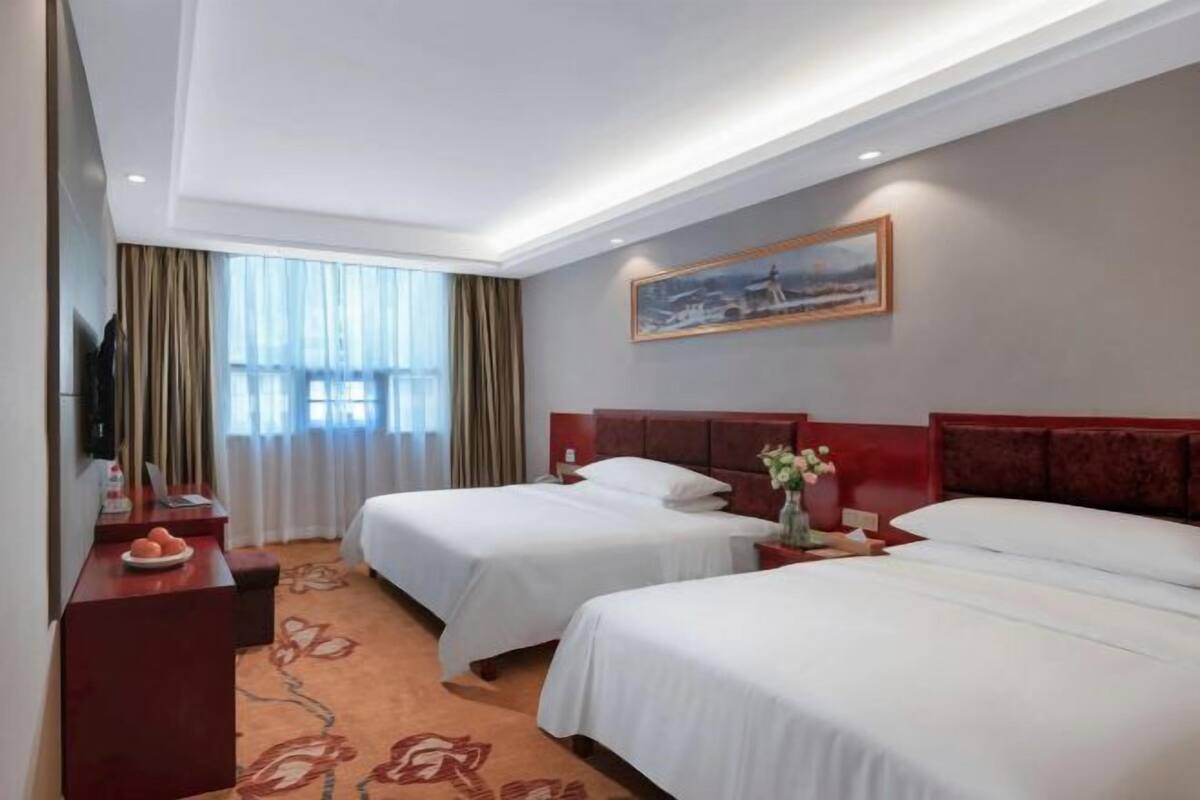 A hotel room with two beds, a desk, a TV, and a painting on the wall.