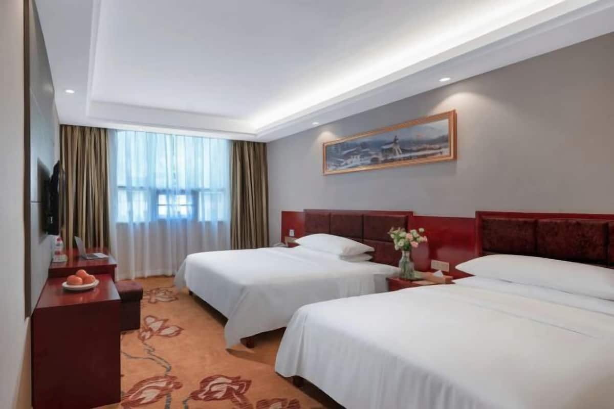 A hotel room with two beds, a desk, a TV, and a painting on the wall.