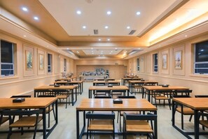 Un comedor espacioso con varias mesas y sillas, una zona de cocina central y obras de arte enmarcadas en las paredes.
