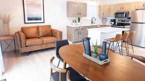 Una cocina moderna con armarios de madera, una isla central y una zona de comedor con mesa y sillas de madera.