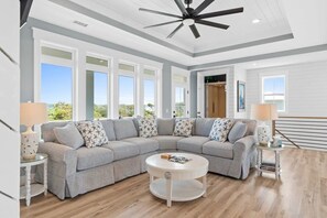 A spacious living room with a sectional sofa, a round coffee table, and a ceiling fan. - Casa Blanca- Ocean Isle Beach (Ocean Isle Beach)