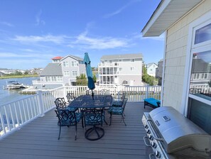 A deck with a table and chairs, a grill, and a view of houses and water. - Colorful Canal-Front Beach House, Beautiful Water Views, & Short Walk to Beach (Bethany Beach)