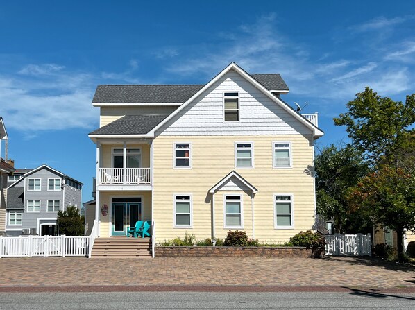 A two-story house with a balcony, a front door, and a small porch with chairs. - Colorful Canal-Front Beach House, Beautiful Water Views, & Short Walk to Beach (Bethany Beach)