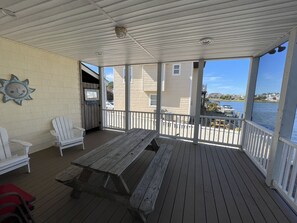 A covered deck with a wooden bench and two Adirondack chairs, overlooking a body of water with boats. - Colorful Canal-Front Beach House, Beautiful Water Views, & Short Walk to Beach (Bethany Beach)
