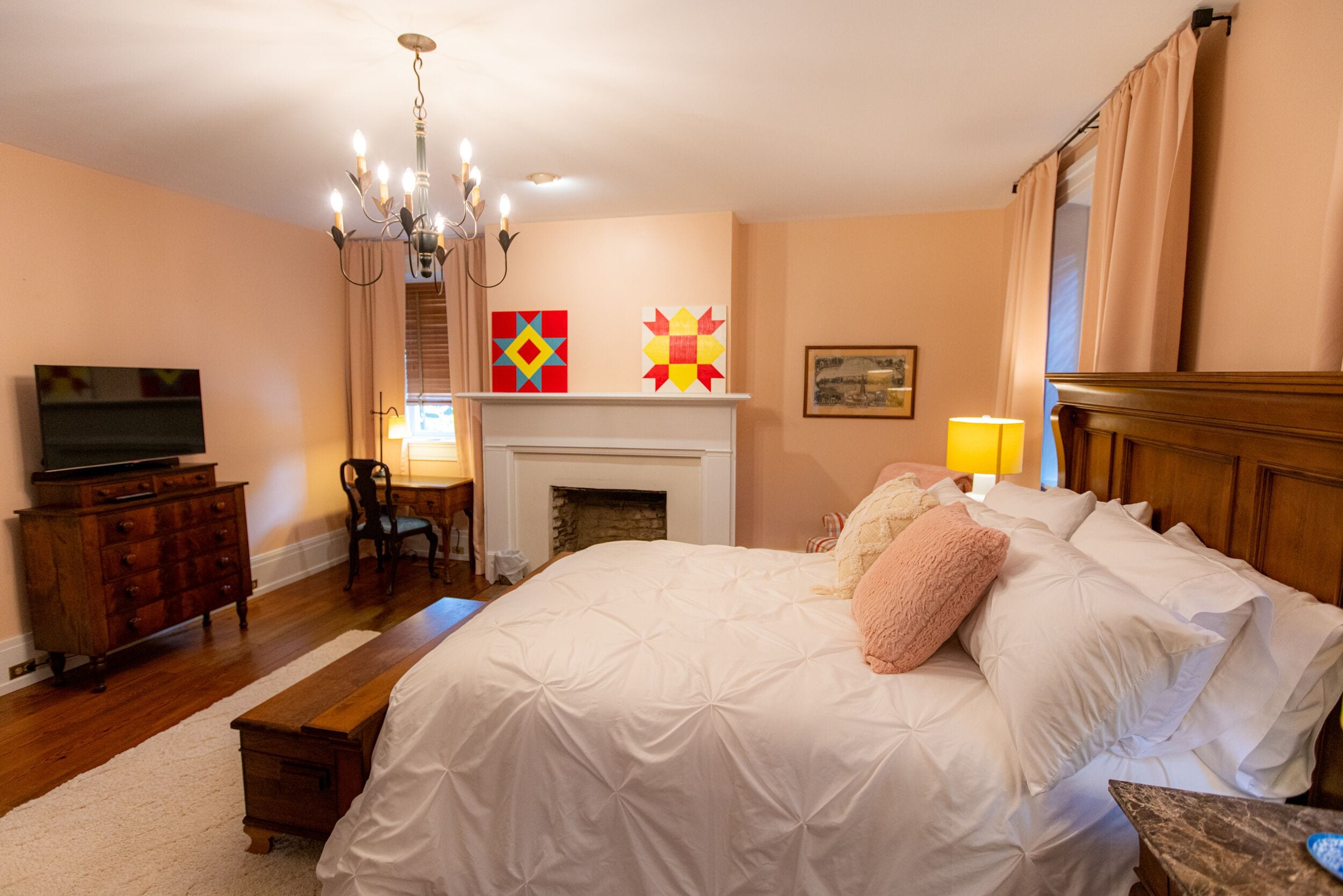 Un dormitorio con una cama grande, un televisor en una cómoda, una chimenea y un candelabro.