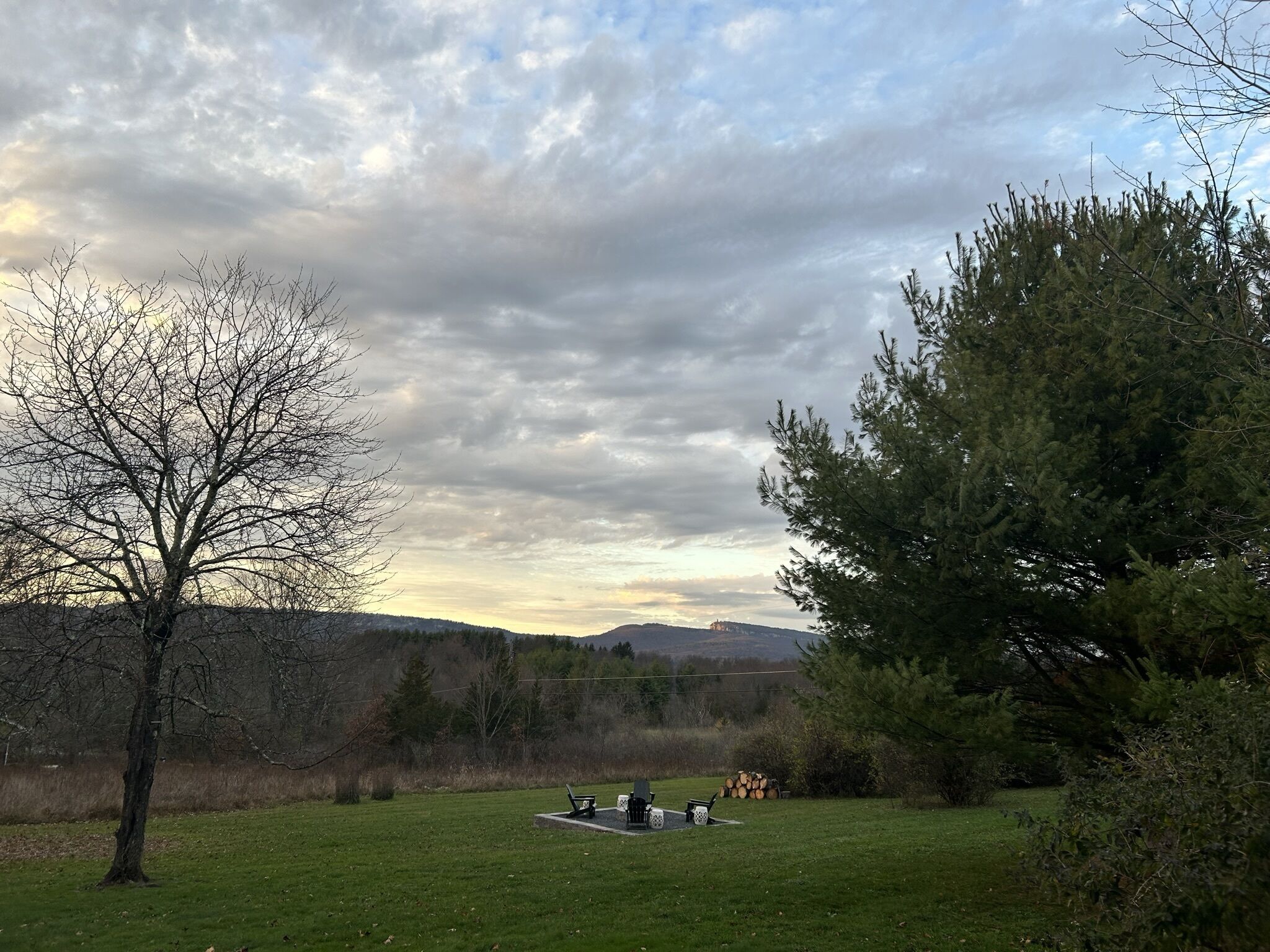 A grassy field with a picnic table and benches, surrounded by trees and a distant mountain range.