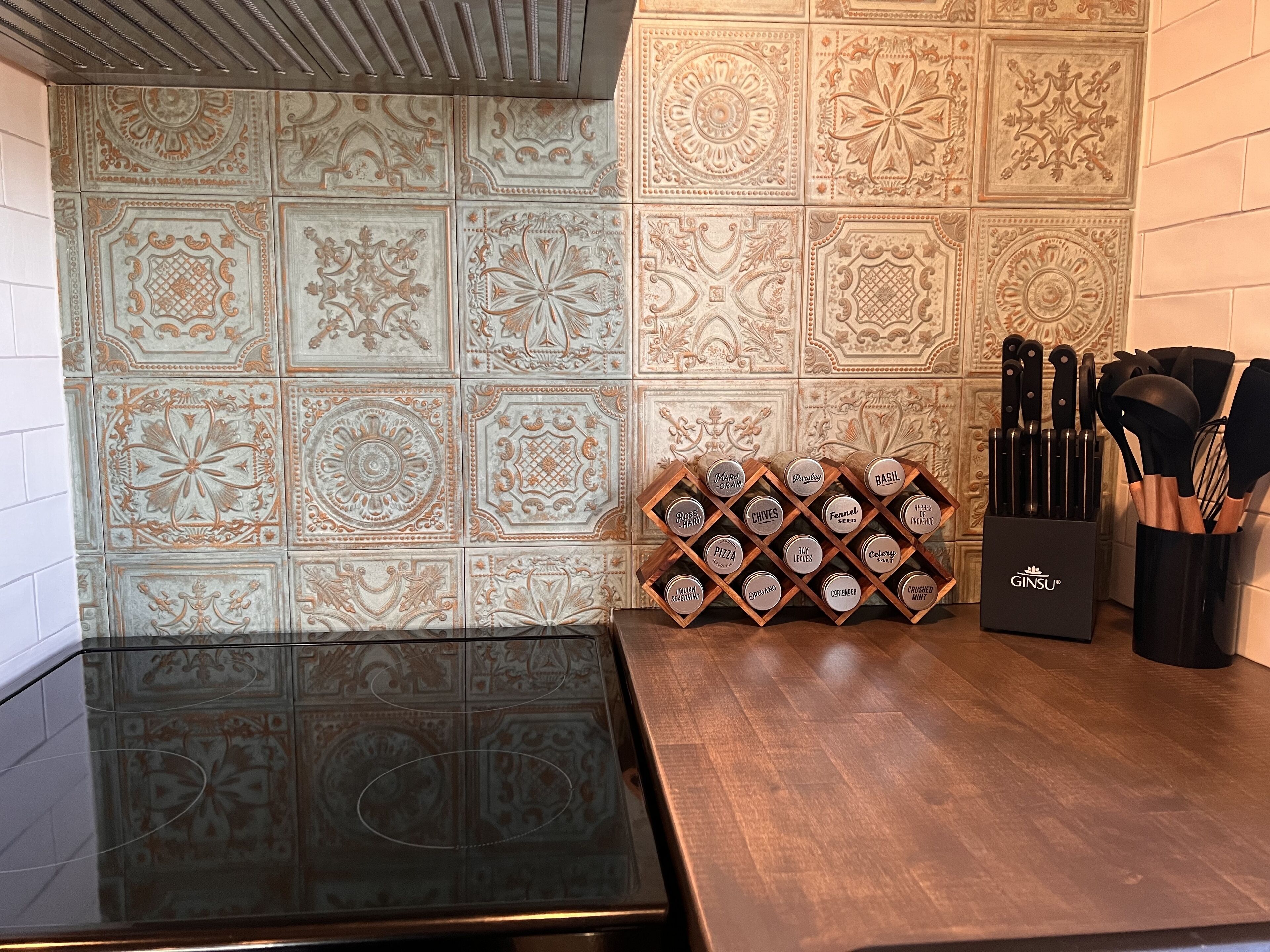 Cozinha com backsplash de azulejos ornamentados, bancada preta e porta-utensílios com facas.