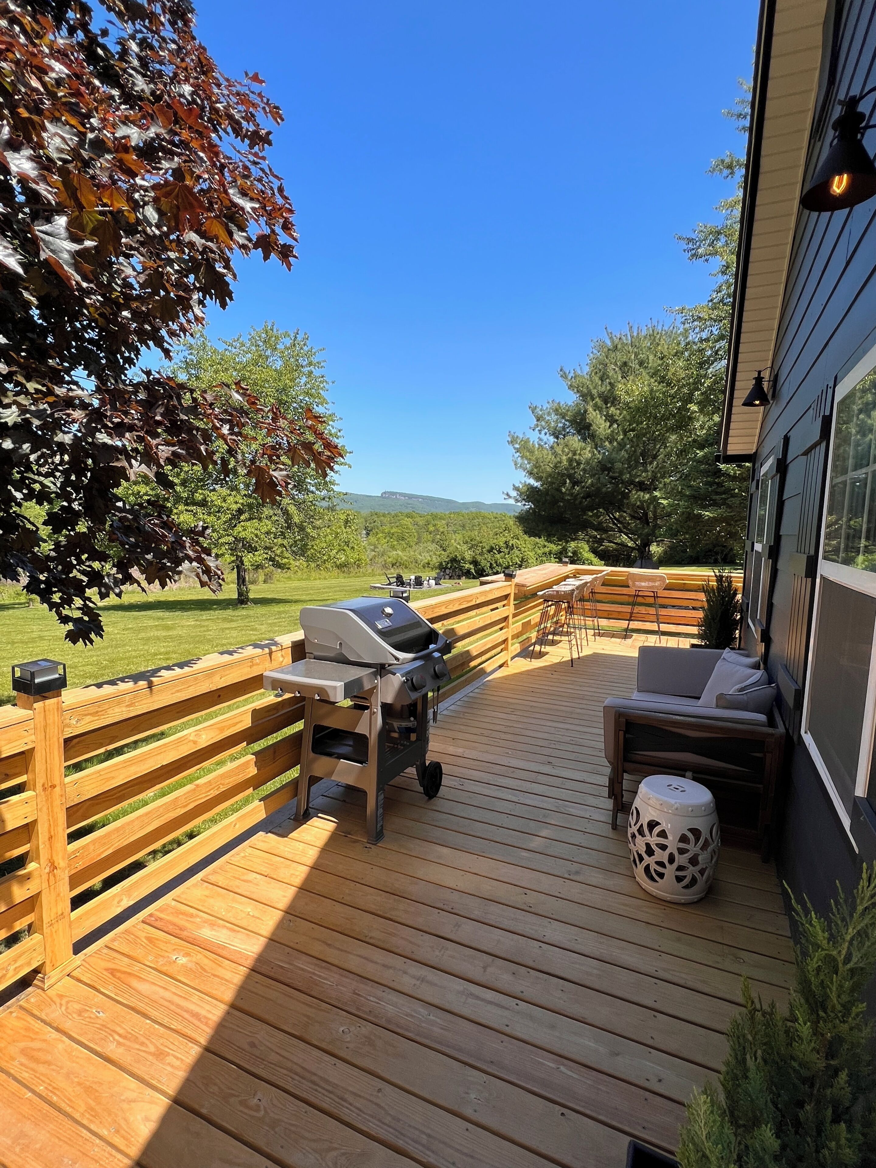 A wooden deck with outdoor furniture, a grill, and a view of the landscape.