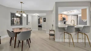 A modern kitchen with white cabinets, a central island, and a dining area with a wooden table and grey chairs.