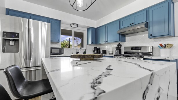 Una cocina moderna con una isla grande de mármol, electrodomésticos de acero inoxidable y armarios azules.