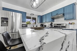 A modern kitchen with a large marble island, stainless steel appliances, and blue cabinetry.