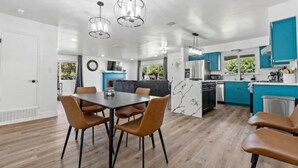 Una cocina moderna con armarios color turquesa, un comedor con mesa y sillas, e iluminación colgante.
