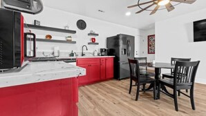 A modern kitchen with red cabinets, a wooden dining table, and black chairs.