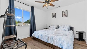 A bedroom with a bed, a ceiling fan, a window with curtains, a ladder, and a small table.