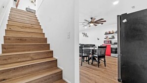A staircase with wooden steps leading to a dining area with a ceiling fan and a black refrigerator.