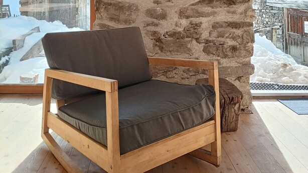 A wooden rocking chair with a cushion, a stone wall, and a clock. - Renovated sheepfold near the slopes ideal for 2 families (CREVOUX)