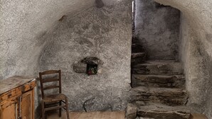 A rustic room with a wooden chair, a wooden cabinet, a stone wall, and a staircase leading to an upper level. - Renovated sheepfold near the slopes ideal for 2 families (CREVOUX)