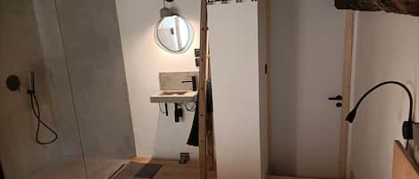 Ett sovrum med en säng, en trädörr, ett litet handfat och en spegel.