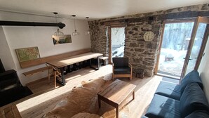 A cozy living room with a stone wall, wooden furniture, and a large window with a snowy view. - Renovated sheepfold near the slopes ideal for 2 families (CREVOUX)
