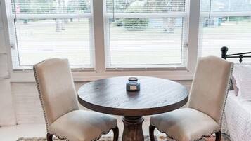 A round wooden table with two upholstered chairs, a woven pendant light, and a colorful rug.