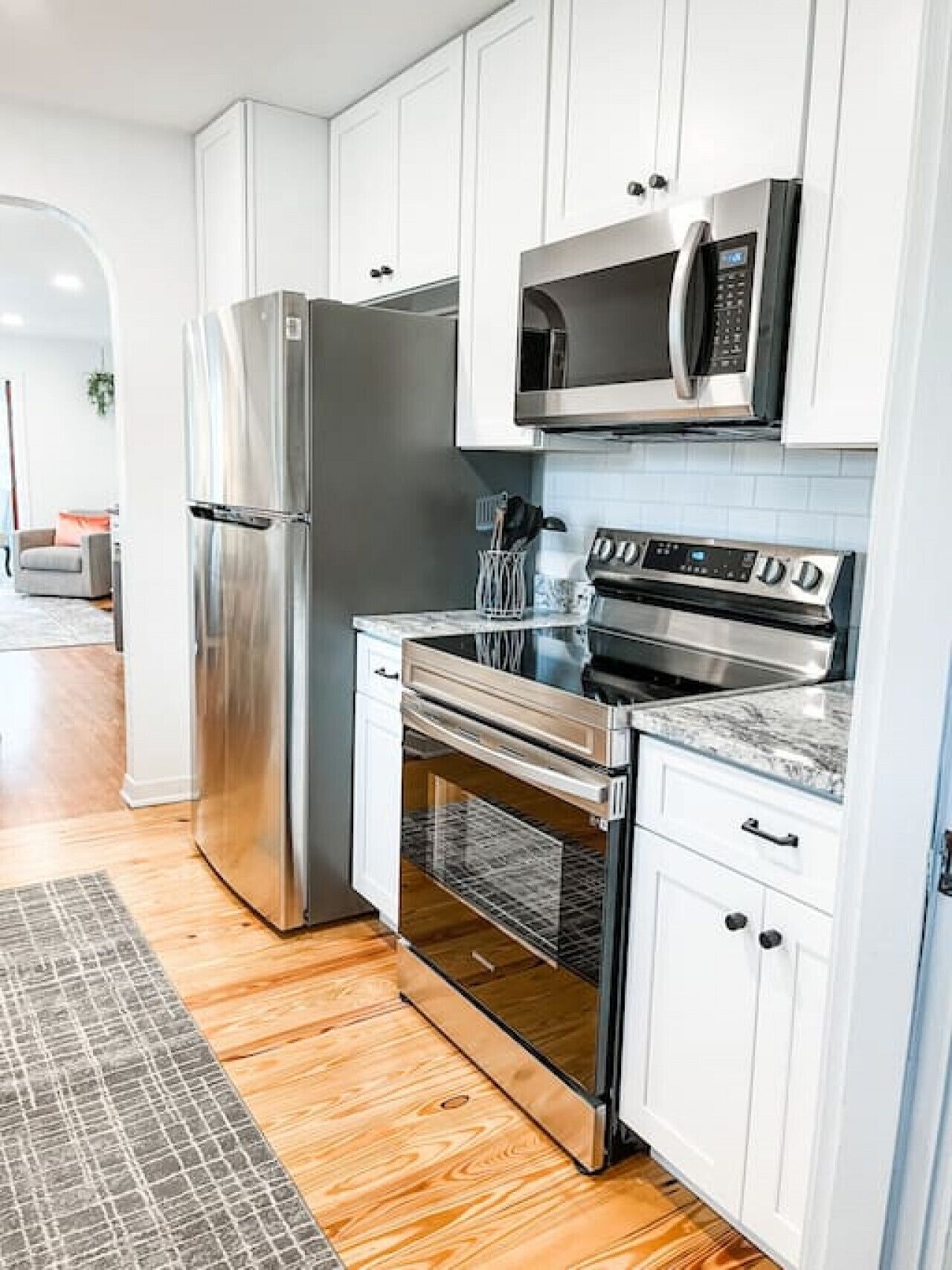 A modern kitchen with stainless steel appliances, white cabinetry, and a patterned rug.
