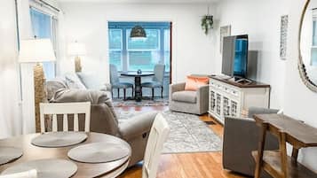 Relax in this inviting living space with a central dining area, sofa, armchair, and large window offering a view of the outdoors.