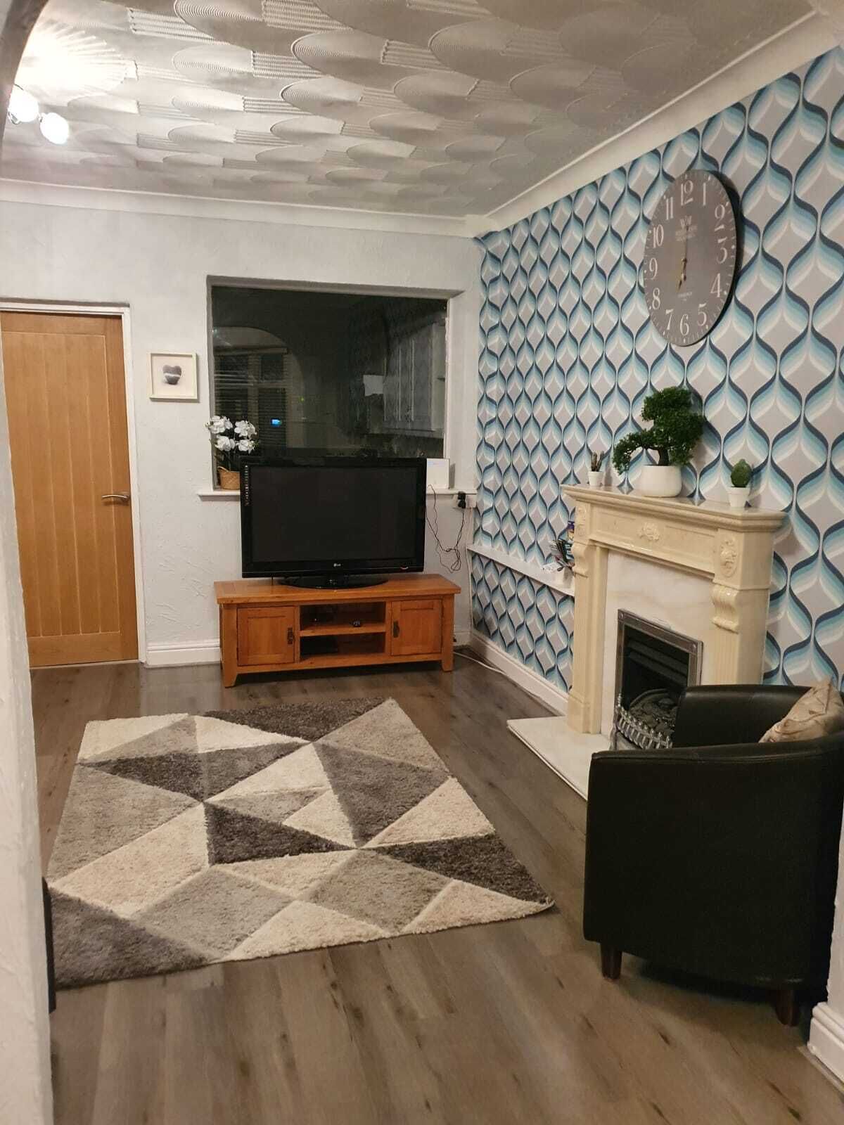 A living room with a fireplace, a television on a wooden stand, and a patterned wall.