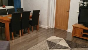 A dining area with a wooden table and chairs, a patterned rug, and a television on a wooden stand. - Waterfalls House - property akin Waterfall Country (Pontneddfechan)