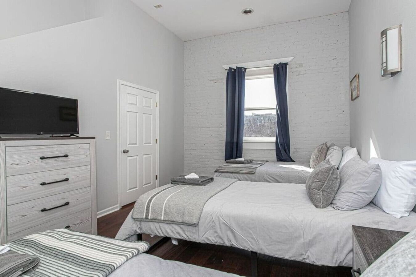 A bedroom with a bed, a dresser, a TV, and a window with curtains.