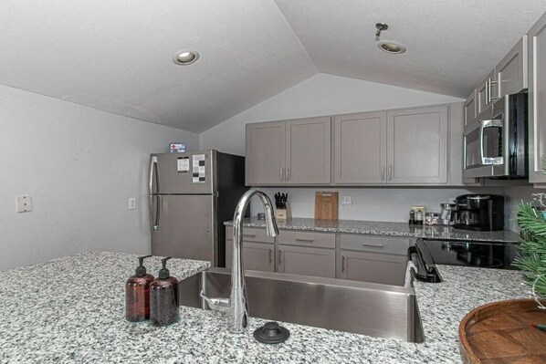 A compact kitchen with granite countertops, stainless steel appliances, and grey cabinets.