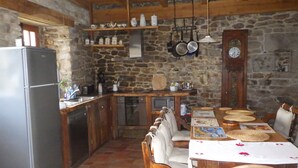 A rustic kitchen with stone walls, wooden cabinets, a refrigerator, a sink, and a dining table with chairs.