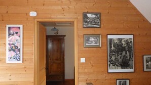 A wooden interior with a hallway leading to a door, framed pictures on the walls, and a ceiling light fixture.