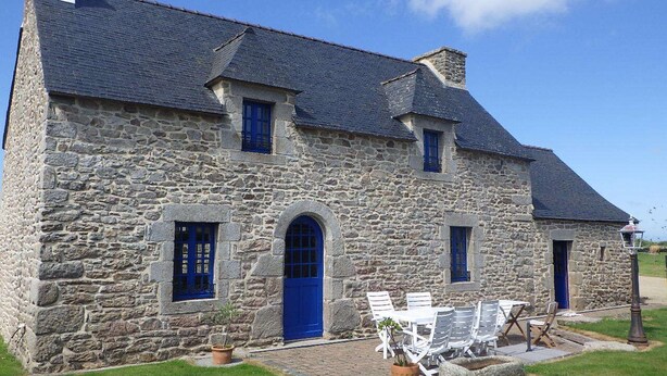 A stone house with a blue door and windows, a small patio with outdoor seating, and a lamp post.