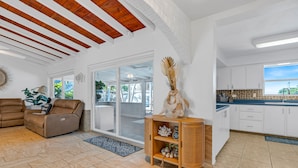 Amplia sala de estar con un sofá de cuero marrón, un mueble de madera con adornos, y vistas a un patio exterior a través de puertas de cristal.