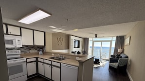 A modern kitchen with a built-in microwave, oven, and dishwasher. There is a large window providing a view of the outdoors. - Paramount Plus/Oceanfront/New (Myrtle Beach)
