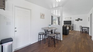 A modern kitchen with a white door, a round dining table with four stools, a TV, and a fireplace. - The Cozy Rustic Sequoia Wi-Fi & 2 Garage (Tulare)