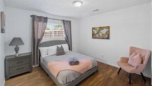 A bedroom with a bed, a nightstand, a chair, a window with curtains, and a wall painting. - The Cozy Rustic Sequoia Wi-Fi & 2 Garage (Tulare)