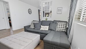 A modern living room with a grey sectional sofa, a grey ottoman, and a black and white checkered throw pillow. - The Cozy Rustic Sequoia Wi-Fi & 2 Garage (Tulare)