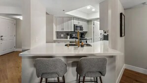 A modern kitchen with white cabinets, a central island with a sink, and two bar stools.