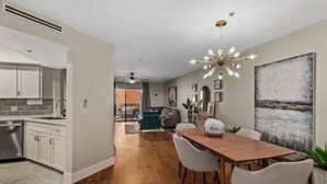 A modern kitchen with white cabinets, a stainless steel dishwasher, and a wooden dining table with white chairs.