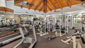 A gym with treadmills, elliptical machines, and weight equipment under a wooden ceiling.