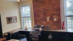 A kitchen with a brick wall, a ceiling fan, a stove, and a dining area with a table and chairs.