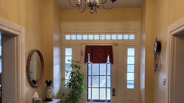 A spacious entryway with a chandelier, a potted plant, a mirror, and a chair.
