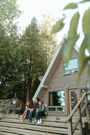 A group of people sitting on outdoor steps in front of a house with a sloped roof and large windows. - A Classic Waterfront A-Frame on Rowley’s Bay (Sister Bay)