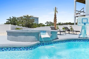 A swimming pool with a built-in basketball hoop, lounge chairs, and a palm tree.