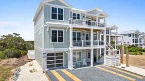 Ein zweistöckiges Strandhaus mit Garage, einem Balkon im oberen Geschoss und freiem Blick auf den Ozean.