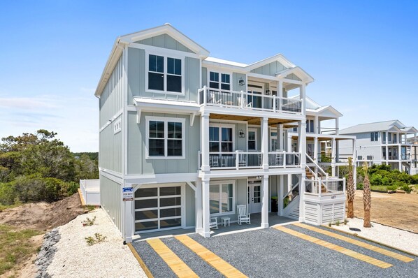 A two-story beachfront property with a garage, a balcony on the upper floor, and a clear view of the ocean.