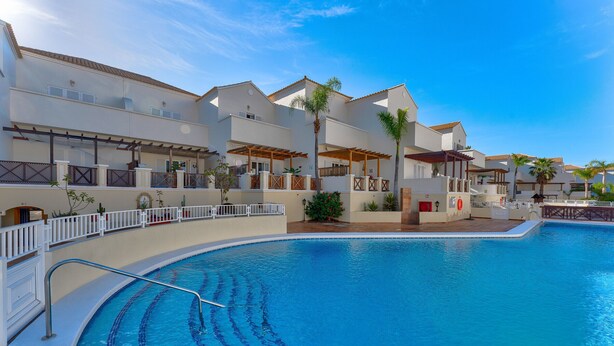 Un resort con una piscina grande, varios balcones y un cielo azul despejado.