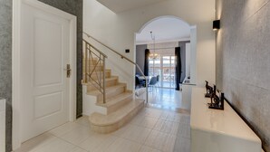 Un interior moderno con una escalera que conduce a un comedor, una recepción y vistas al exterior.