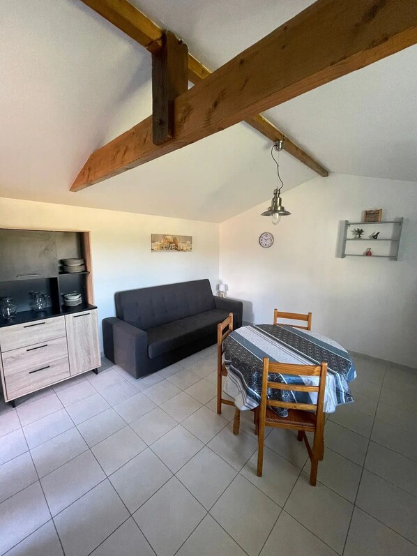 A compact living space with a kitchenette, a sofa, a dining table, and a ceiling with exposed wooden beams. - ADORABLE STUDIO NEAR THE SEA (Talais)